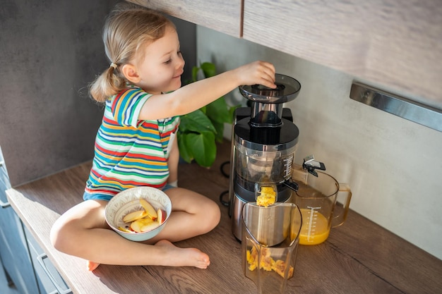 Little girl making fresh juice sitting on the table in home kitchen