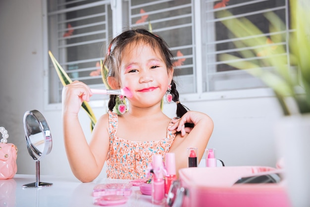 Little girl making makeup her face she look in the mirror and cheek fluffy brush for powder