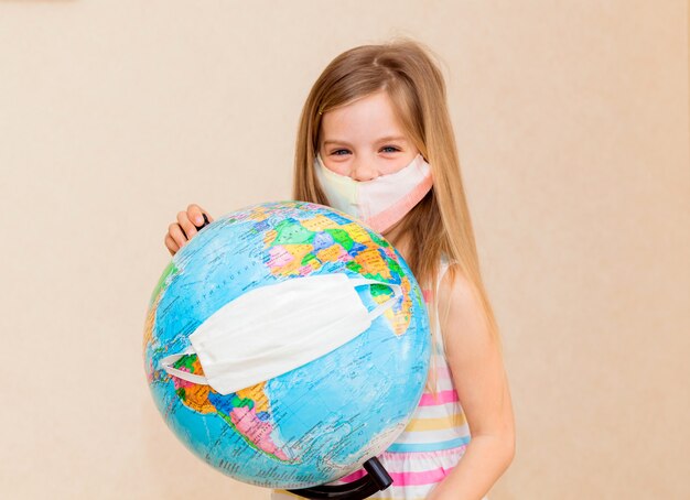 Little girl in a medical mask holds a globe in her hands, wrapped in a medical mask. 