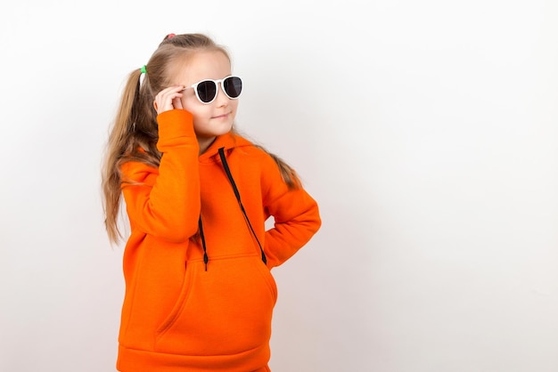 A little girl in an orange hoody and sunglasses emotions of joy and a sunny day portrait On a white background