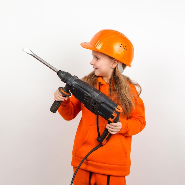 Little girl in an orange suit and construction helmet holding puncher concept of young worker Portrait child builder white background Labor Day