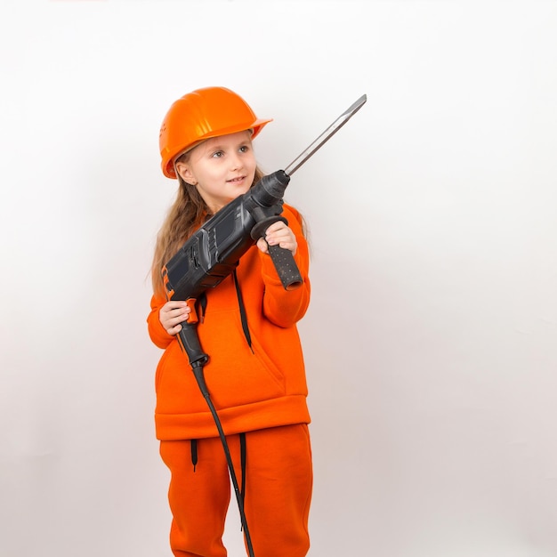 Little girl in an orange suit and construction helmet holding puncher concept of young worker Portrait child builder white background Labor Day