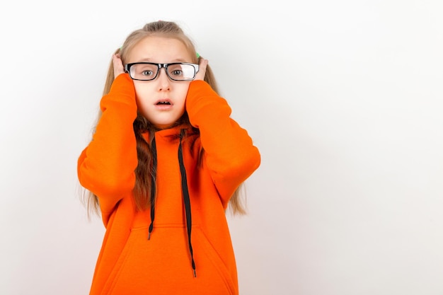 A little girl in an orange suit and eyeglasses Emotions a portrait on a white background