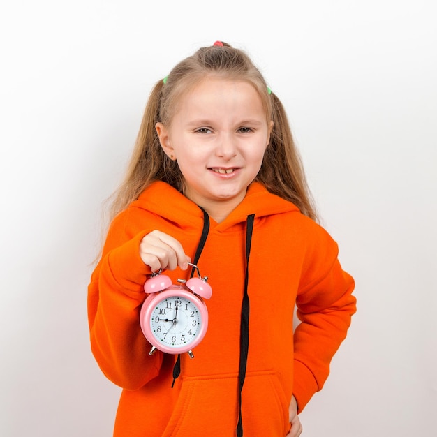 A little girl in an orange suit holds an alarm clock Concept the time has come it's time for school