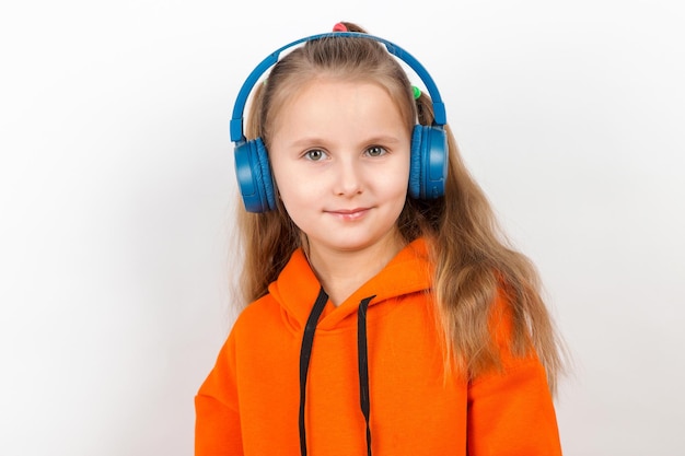 A little girl in an orange suit listening to music in blue headphones on white background