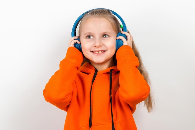 A little girl in an orange suit listening to music in blue headphones on white background