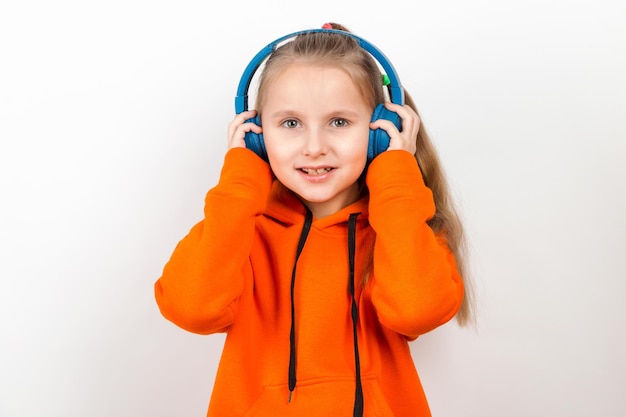 A little girl in an orange suit listening to music in blue headphones on white background