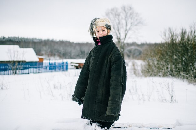 Little girl in oversized jacket standing on snow in winter