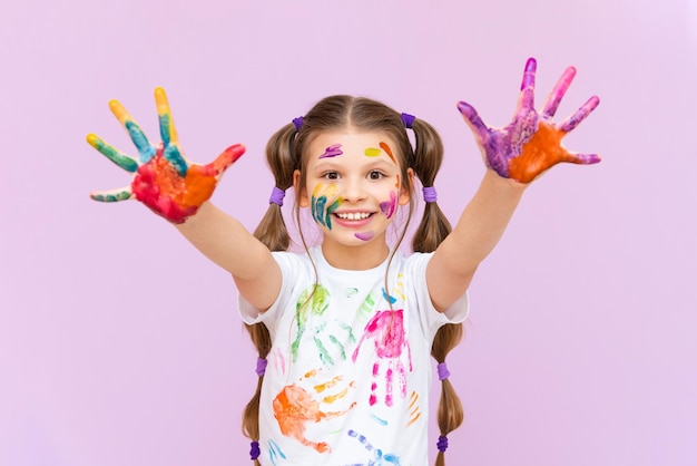 A little girl painted with multicolored paints will playfully have to create on a pink isolated background Development of children's creativity for schoolchildren