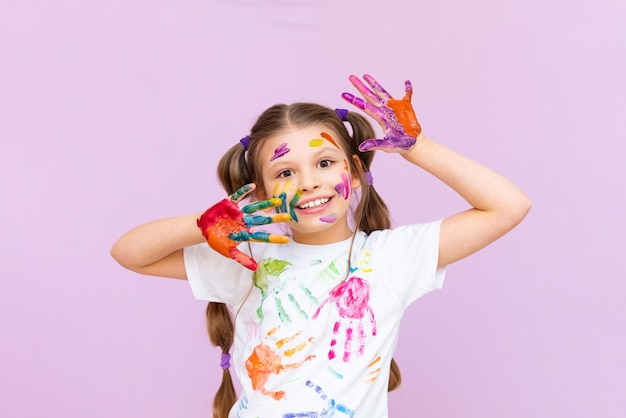 A little girl painted with multicolored paints will playfully have to create on a pink isolated background Development of children's creativity for schoolchildren