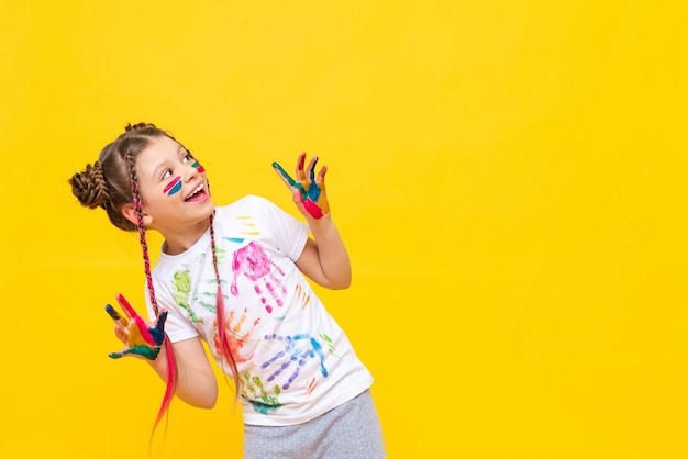 A little girl painted with paints looks at your advertisement on a yellow isolated background The art of painting with paints for children Art courses for schoolchildren Copy space