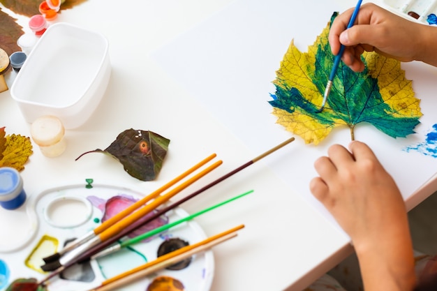 Photo little girl painting on autumn yellow leaves with gouache, kids arts, children creativity, autumn art.