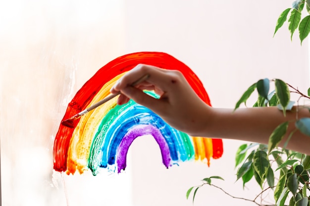 Little girl painting rainbow on window