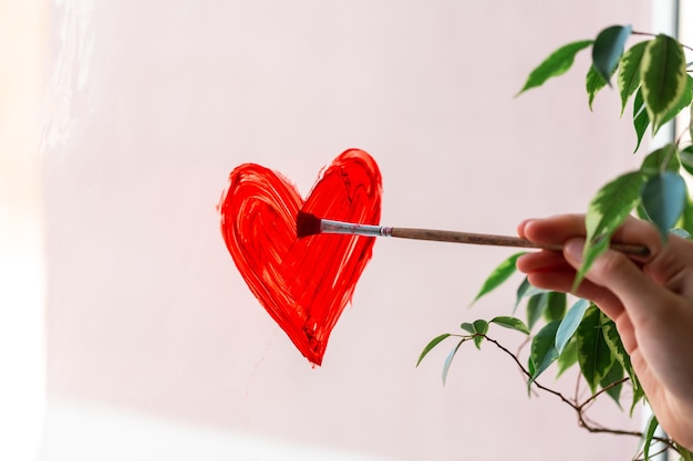 Little girl painting red heart on window