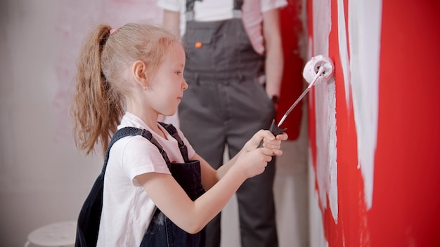 A little girl painting wall with a paint roller