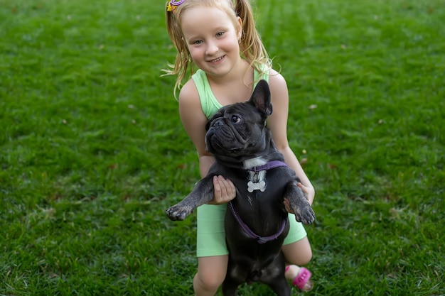 Little girl in the park trying to pick up a french bulldog