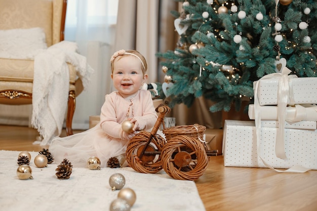 Little girl in peach dress sitting near christmas tree at home