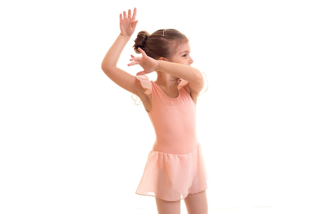 Little girl in pink dress dancing on white background in studio