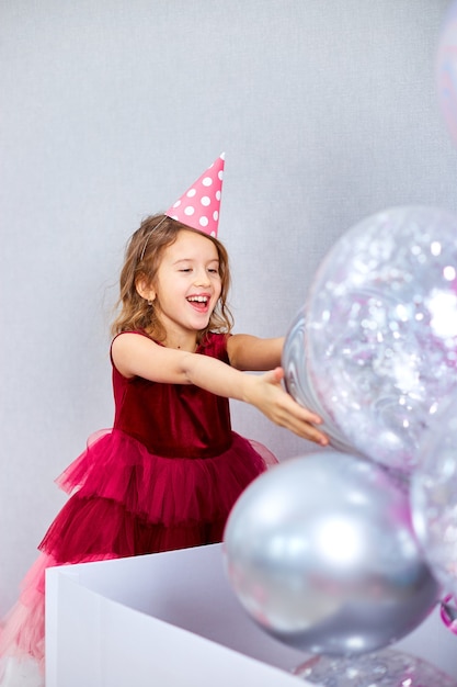 little girl in pink dress and hat open big present gift box with balloons home birthday party