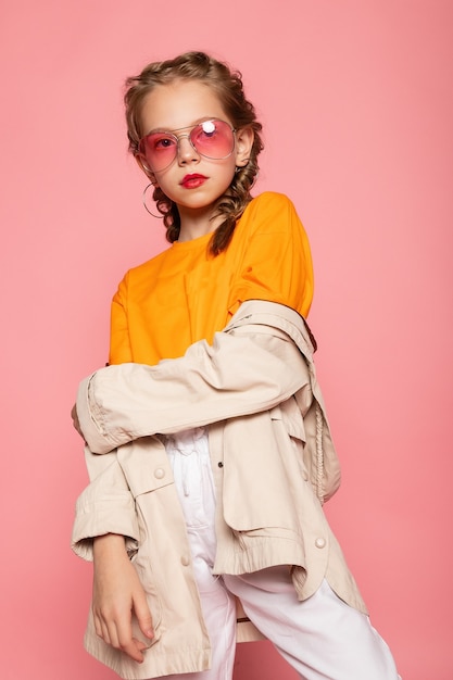 Little girl in pink glasses. Trendy fashion style stylish funtime concept. Vertical full-size full-length portrait of laughing cute sweet adorable lovely charming girl isolated pink wall