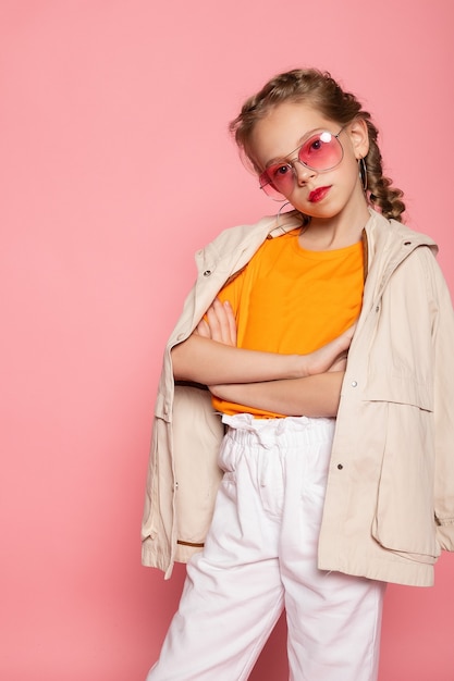 Little girl in pink glasses. Trendy fashion style stylish funtime concept. Vertical full-size full-length portrait of laughing cute sweet adorable lovely charming girl isolated pink wall