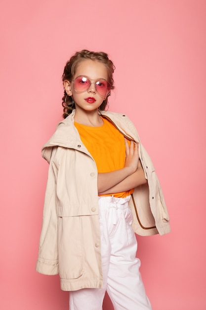 Little girl in pink glasses. Trendy fashion style stylish funtime concept. Vertical full-size full-length portrait of laughing cute sweet adorable lovely charming girl isolated pink wall