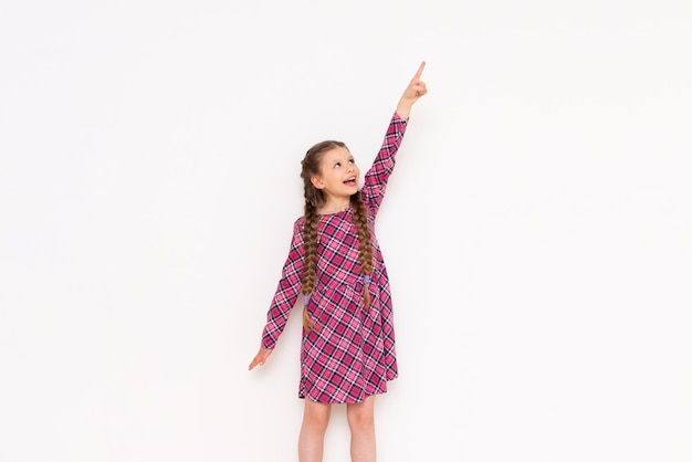 A little girl in a pink plaid dress points to your advertisement on a white isolated background