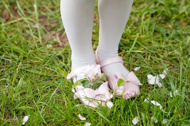 Little girl in pink shoes on green grass in the blossoming park. Close-up feet.