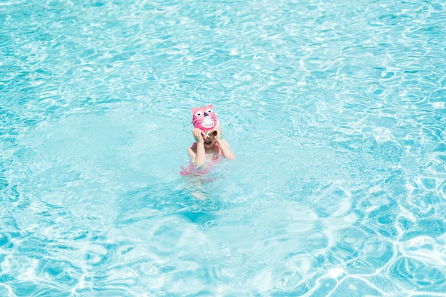 Little girl in pink swim cup and goggles swimming in outdoor pool in the Summer.