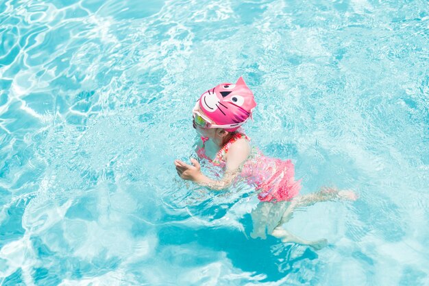 Little girl in pink swim cup and goggles swimming in outdoor pool in the Summer.