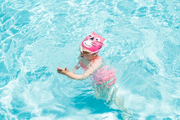 Little girl in pink swim cup and goggles swimming in outdoor pool in the Summer.