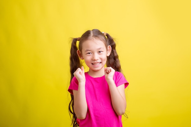 A little girl in a pink Tshirt is happy on a yellow background