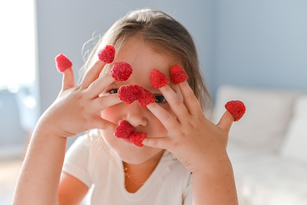 The little girl played with raspberries on her fingers