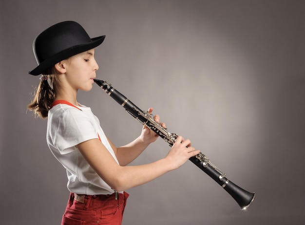 Little girl playing clarinet on gray