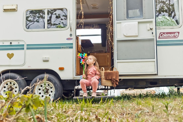 Little girl playing on the steps of a travel trailer with a windmills