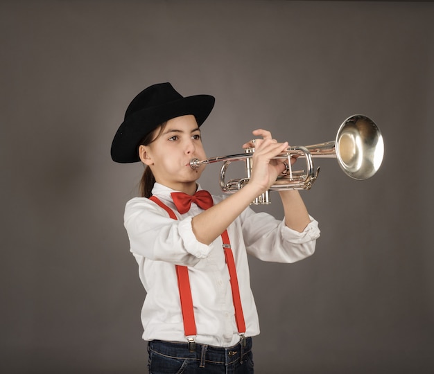 Little girl playing trumpet on gray