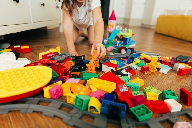 Little girl playing with colorful toy blocks. Educational and creative toys and games for young children. Playtime and mess in kid's room