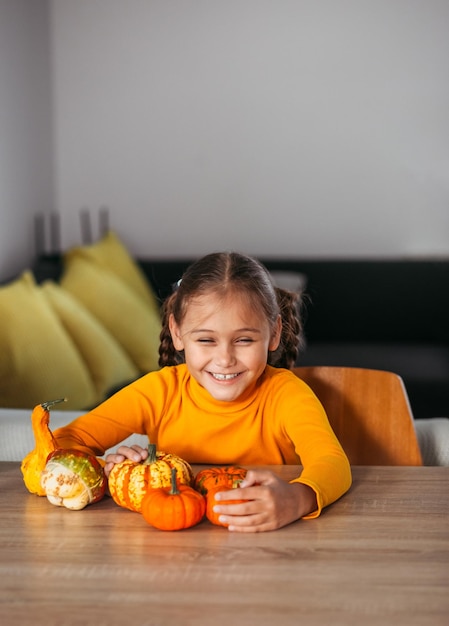 Little Girl Playing With a Pumpkin emotional portrait at home Halloween party concept Vertical