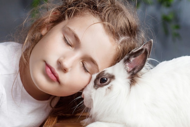 Little girl playing with real rabbit. Child and white bunny on Easter. Kid kiss pet. Fun and friendship for animals and children.