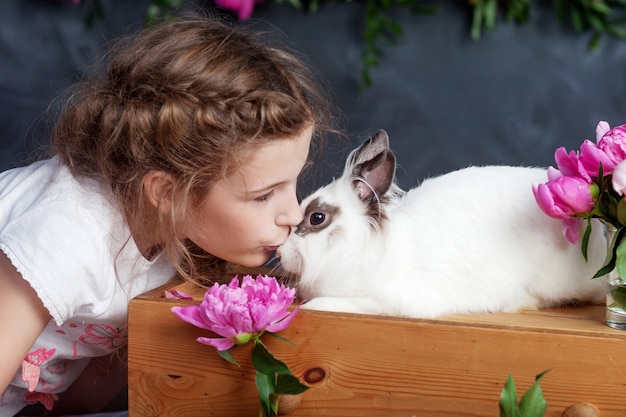 Little girl playing with real rabbit. Child and white bunny on Easter. Kid kiss pet. Fun and friendship for animals and children.