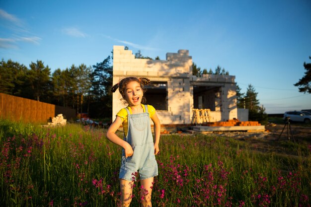 A little girl plays and dances near the construction site of her future house in the countryside. Waiting for a move, dreams of future housing. Mortgage, construction loan.