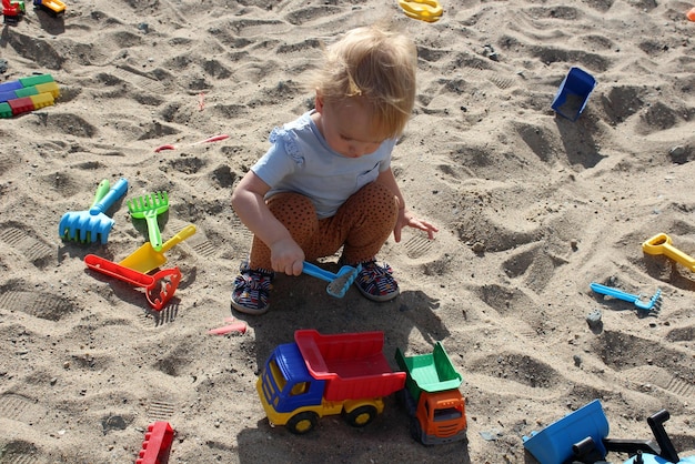 Little girl plays in the sandbox with toys