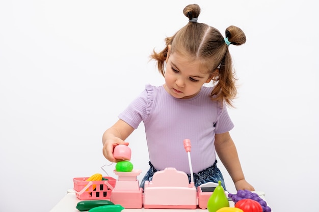 Little girl plays in the store scans and weighs vegetables on toy scales children's cash register closeup children's home games concept