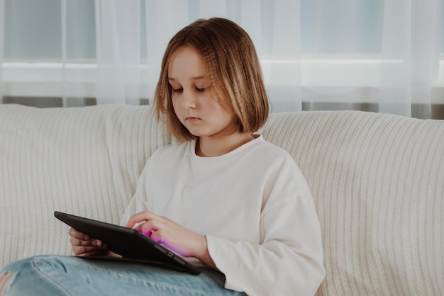 Little girl plays in a tablet on the couch