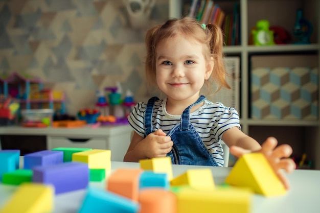 The little girl plays with colorful toy blocks and builds a tower Educational and creative toys and games for young children