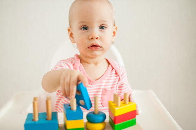 Little girl plays with an educational toy - a multi-colored wooden pyramid. Development of fine motor skills and logical thinking. High quality photo