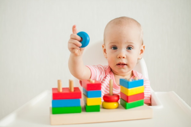 little girl plays with an educational toy - a multi-colored wooden pyramid. Development of fine