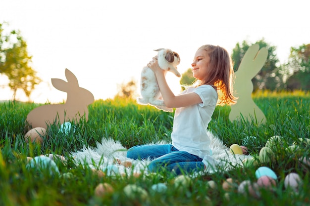 Little girl plays with the rabbit surrounded by Easter eggs