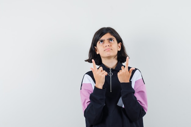 Little girl pointing fingers up in shirt and looking doubtful. front view.