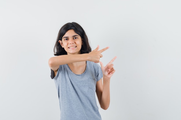 Little girl pointing to the right side in t-shirt and looking merry , front view.